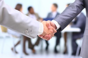 Two successful businessman shaking hands in front of corporate team at office